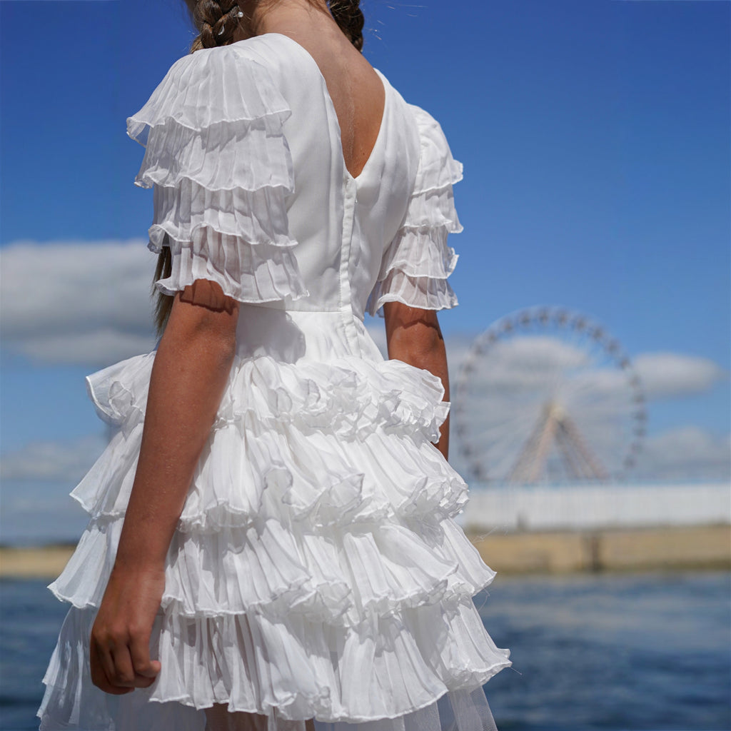 Robe enfant blanche élégante avec manches volantées et jupe asymétrique fluide.