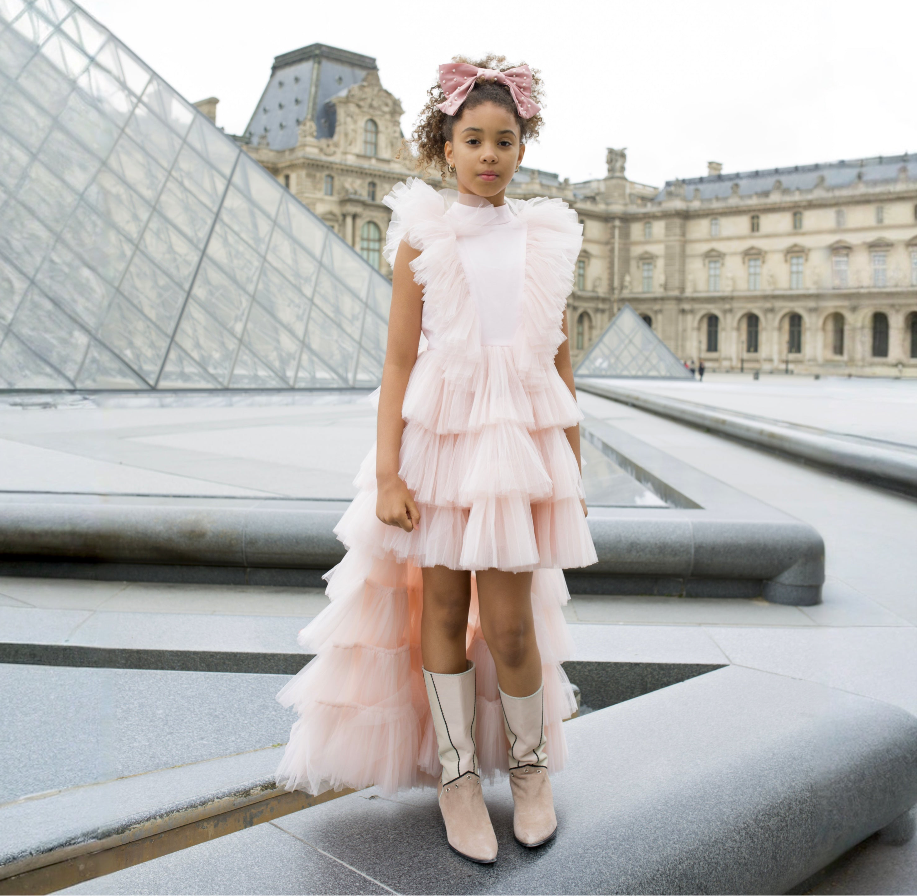 Petite fille portant une robe de cérémonie rose poudré en tulle devant le musée du Louvre à Paris