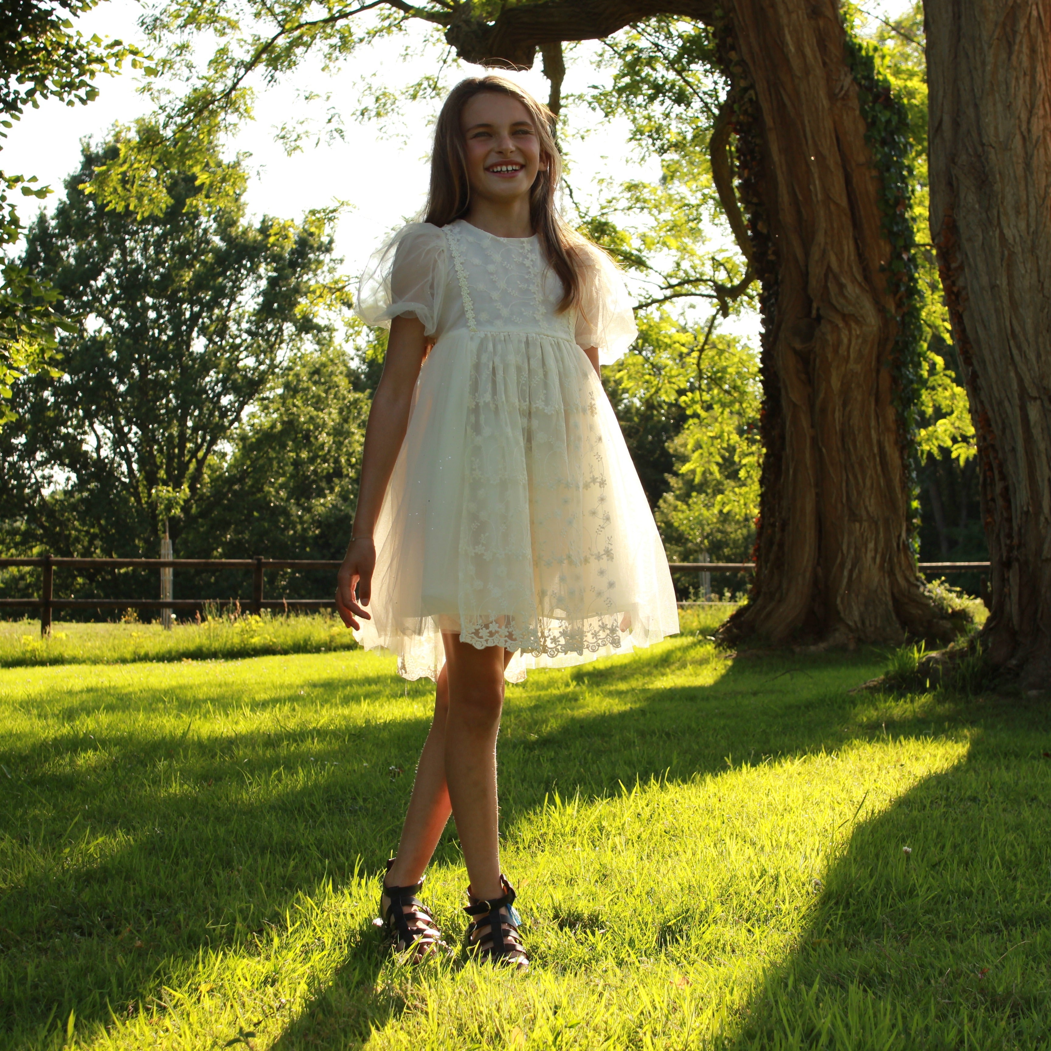 Fille portant une robe de cérémonie en tulle ivoire brodé avec manches ballon dans un jardin d’été