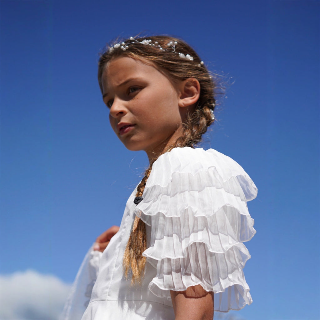 Jeune fille portant une robe blanche à volants avec traîne en tulle, ambiance marine chic.