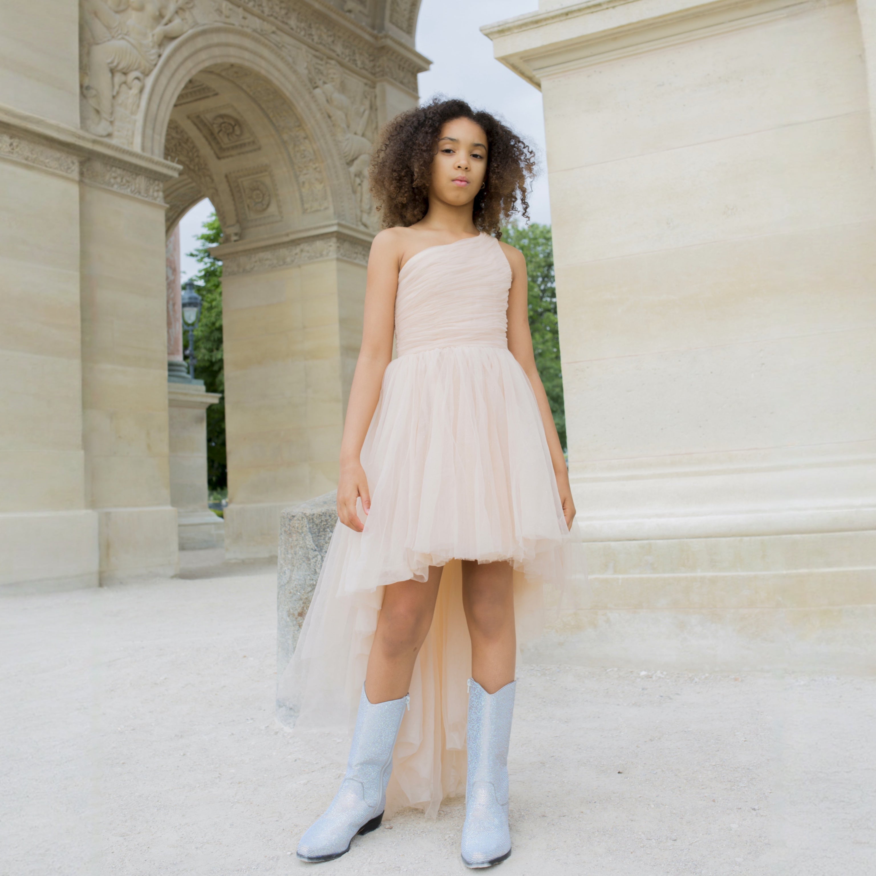 Fille portant une robe de cérémonie nude une épaule avec jupe en tulle asymétrique, look chic et tendance.