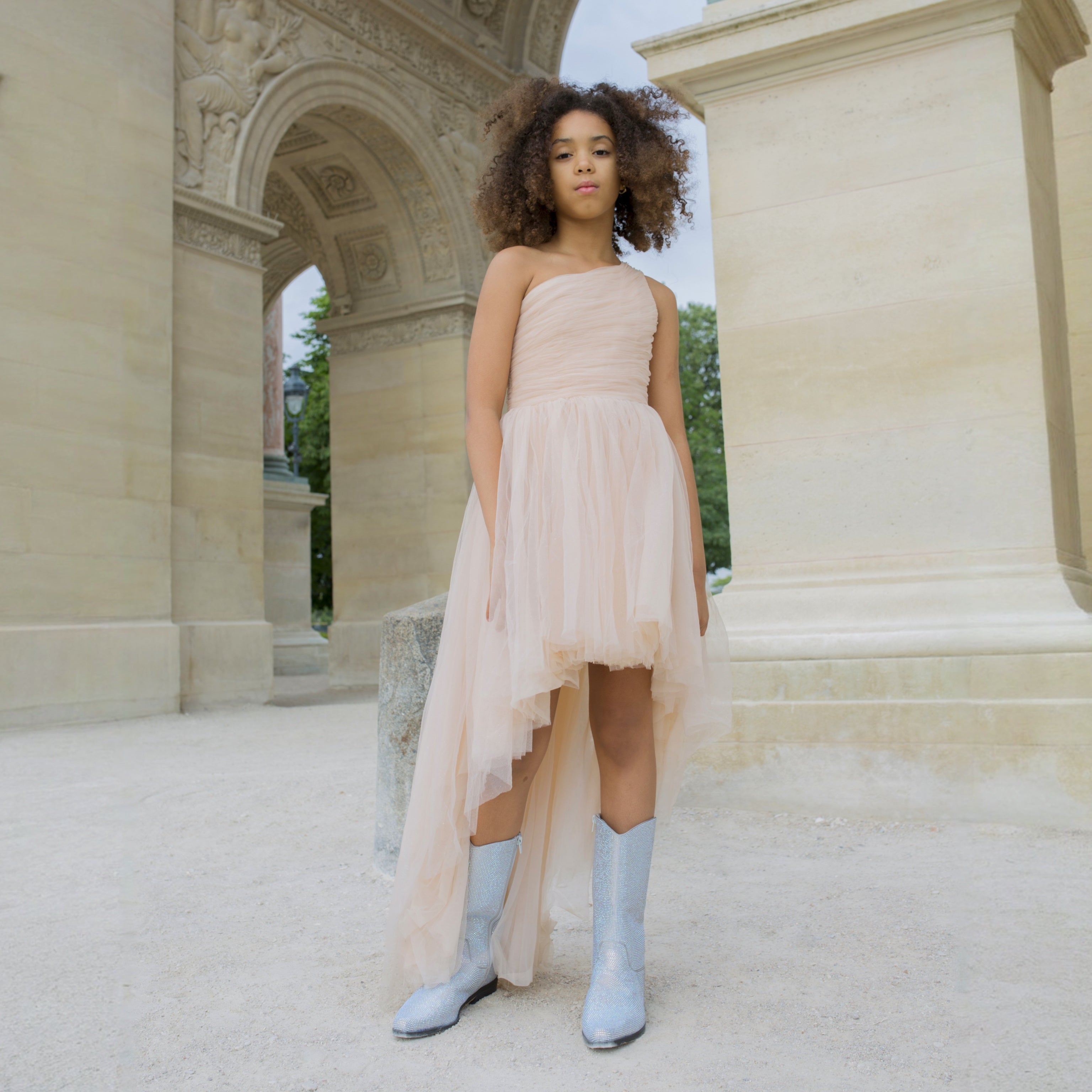 Fille portant une robe de cérémonie nude une épaule avec jupe en tulle asymétrique, look chic et tendance.