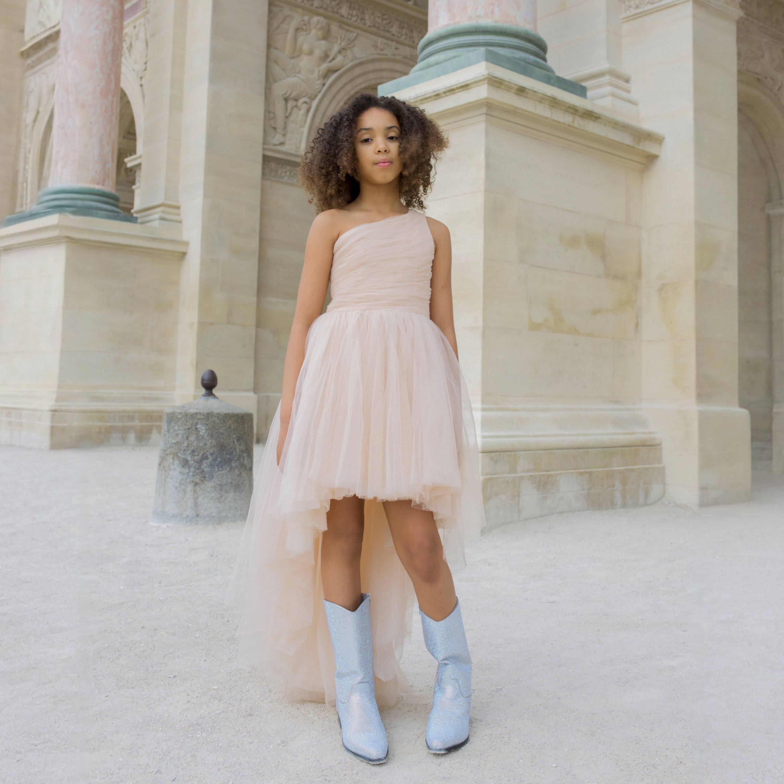 Fille portant une robe de cérémonie nude une épaule avec jupe en tulle asymétrique, look chic et tendance.