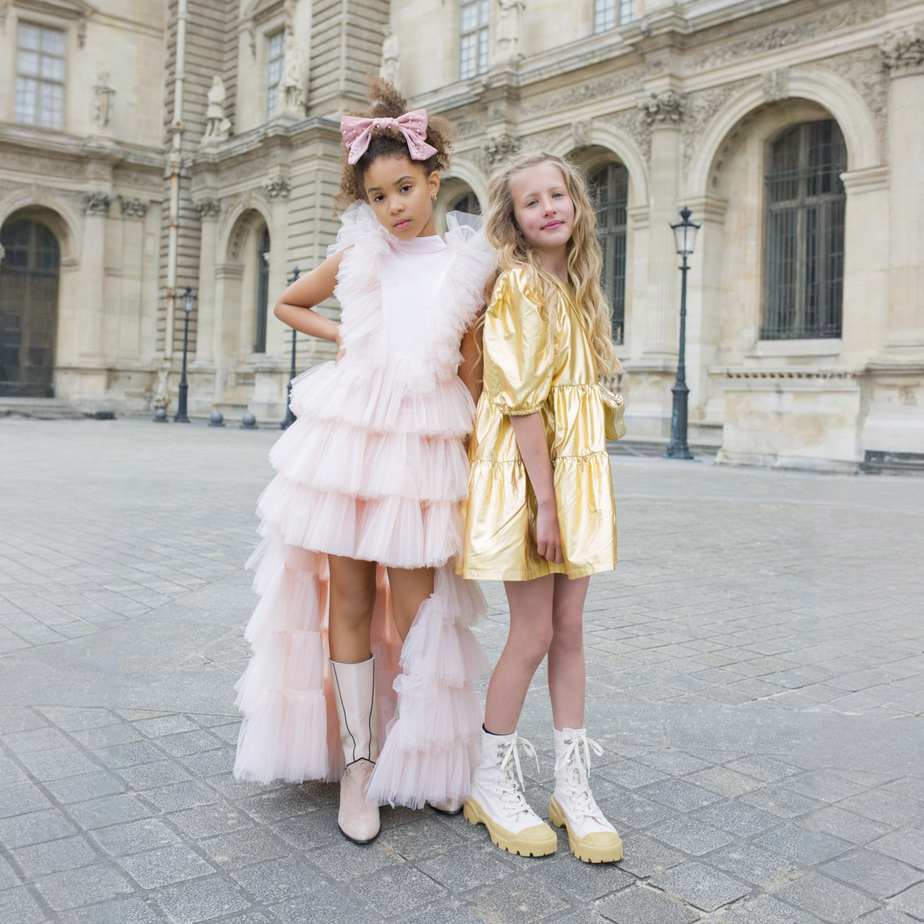 Petite fille portant une robe de cérémonie rose poudré en tulle devant le musée du Louvre à Paris